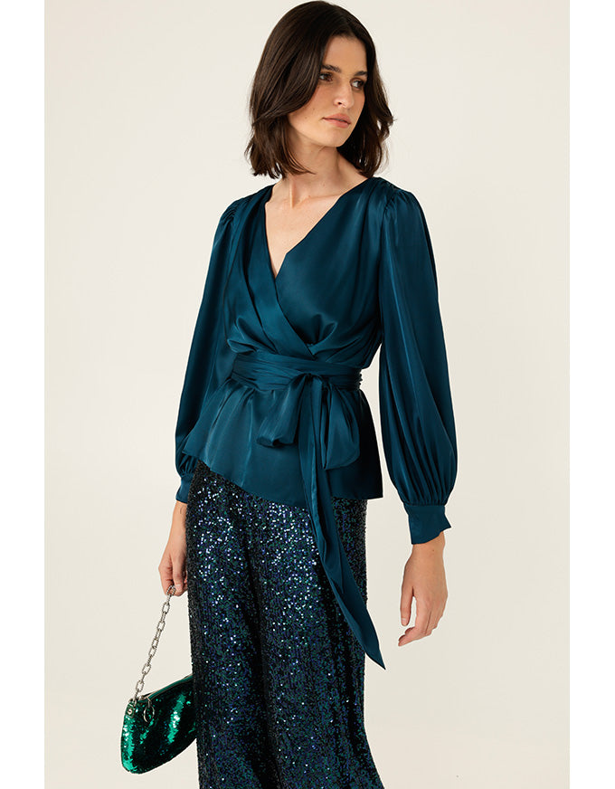 Woman wearing a teal satin top and sequin pants with a neutral background