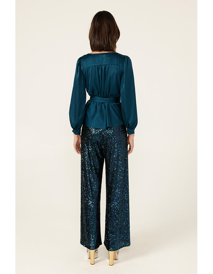 Woman wearing a teal top and patterned pants on a white background