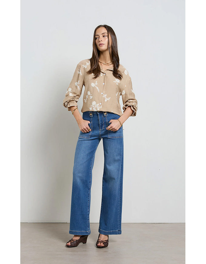 Woman wearing a beige floral blouse and blue jeans against a plain background