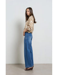 Woman wearing a beige floral blouse and blue jeans against a white background