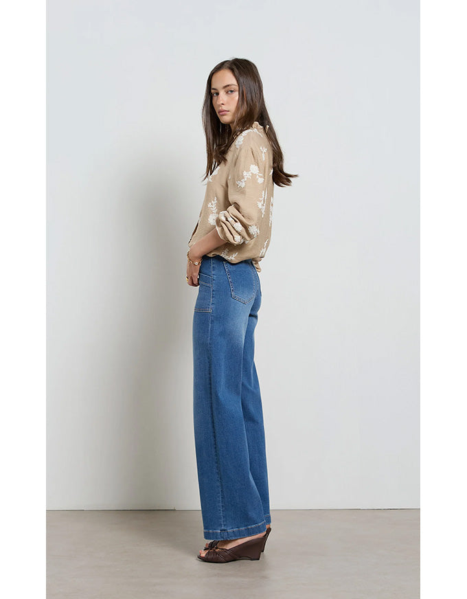 Woman wearing a beige floral blouse and blue jeans against a white background