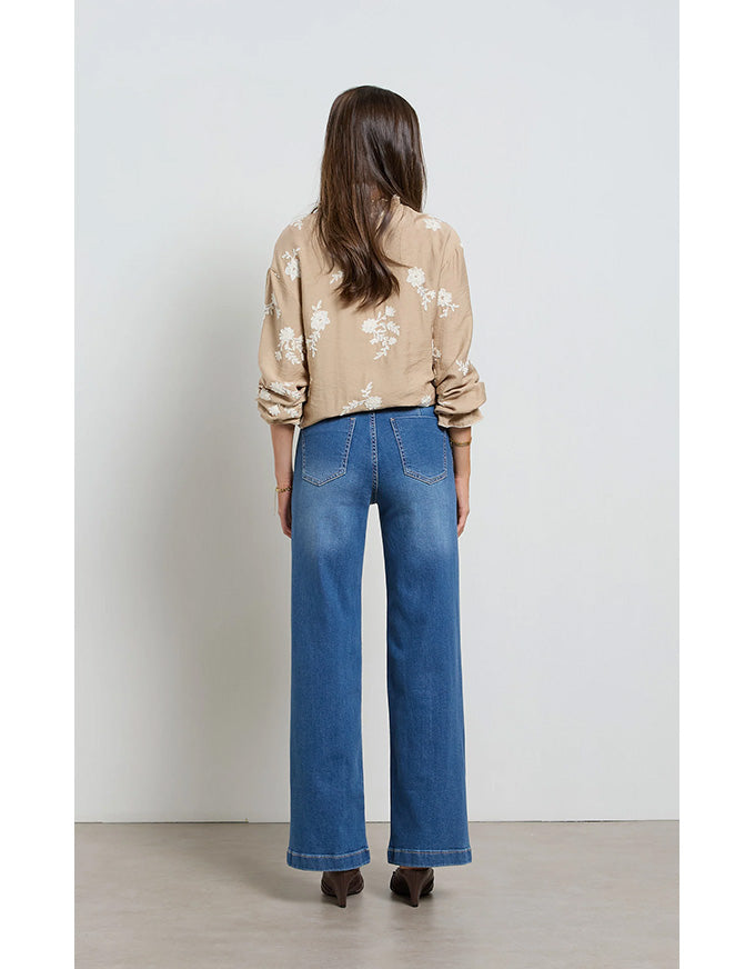 Woman wearing a beige floral shirt and blue jeans against a white background