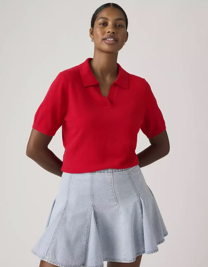 Woman wearing a red polo shirt and light blue denim skirt on a plain background