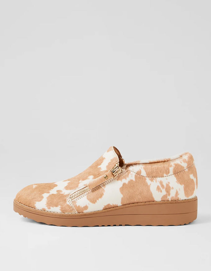 Tan and white cow print slip-on shoe on a light gray background