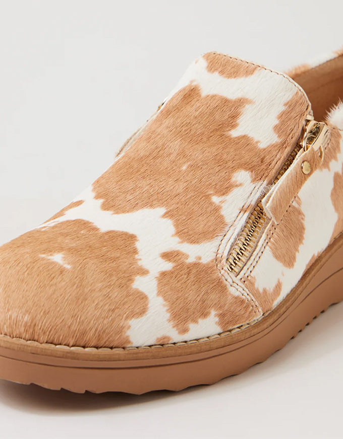 Brown and white cow print slip-on shoe on a light gray background