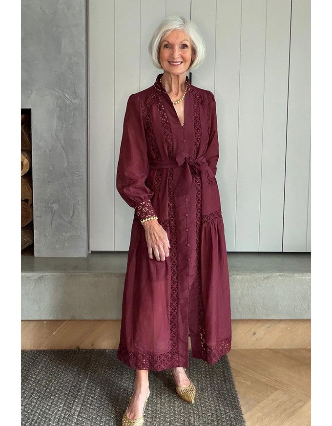 Woman in a burgundy dress standing in a room with wooden flooring and a fireplace.