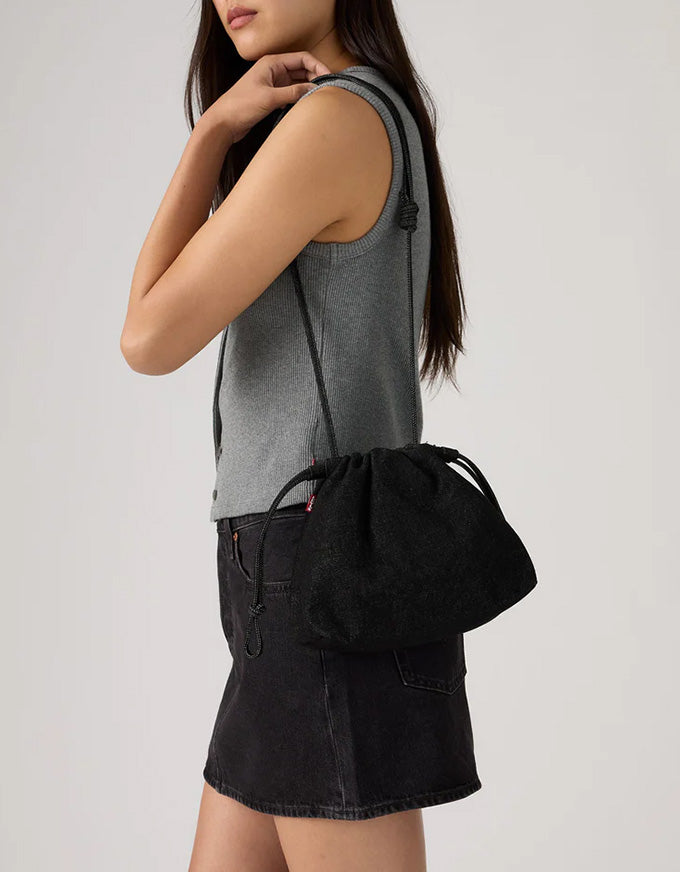 Woman wearing a gray sleeveless top and black denim skirt with a black drawstring bag over her shoulder on a plain background.
