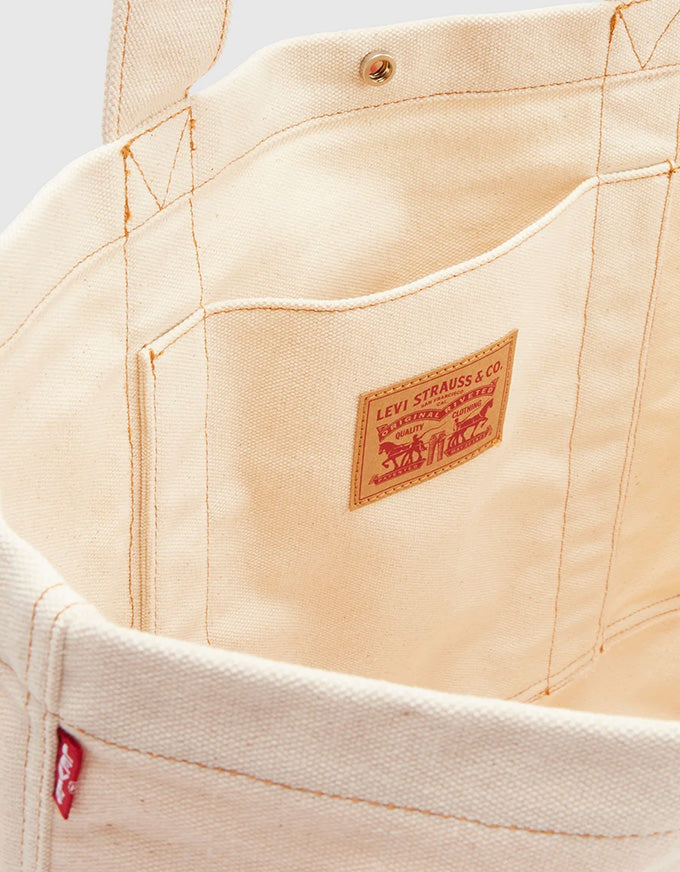 Close-up of the interior of a canvas tote bag by Levi's, showing a cream-colored fabric body, a front pocket, and the signature red and brown Levi's brand patch sewn onto the pocket.