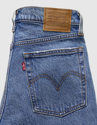 Close-up of the back waistband and rear pocket of blue Levi's jeans, showing the brown leather brand patch and the signature red tab.
