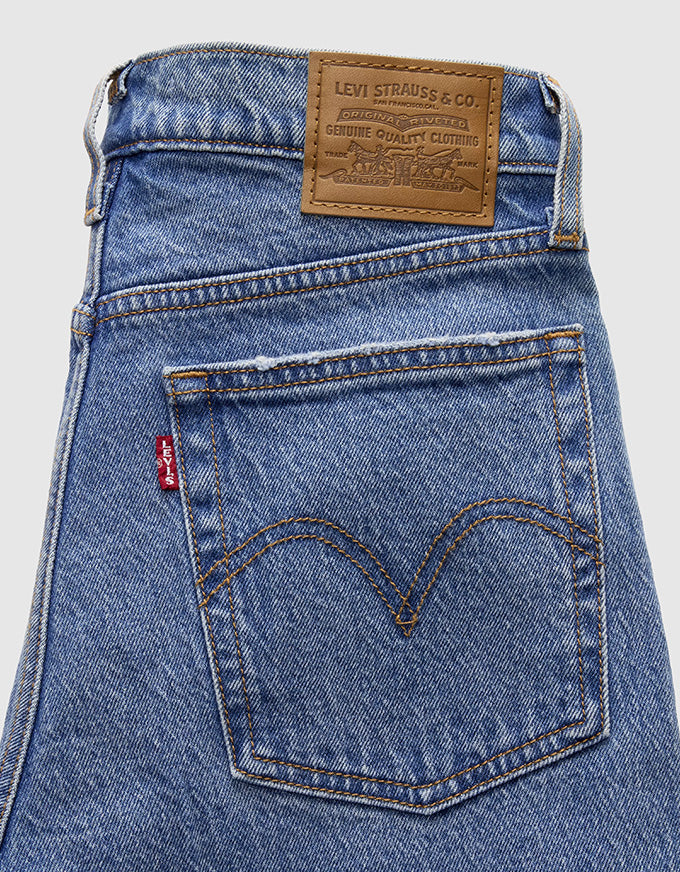 Close-up of the back waistband and rear pocket of blue Levi's jeans, showing the brown leather brand patch and the signature red tab.