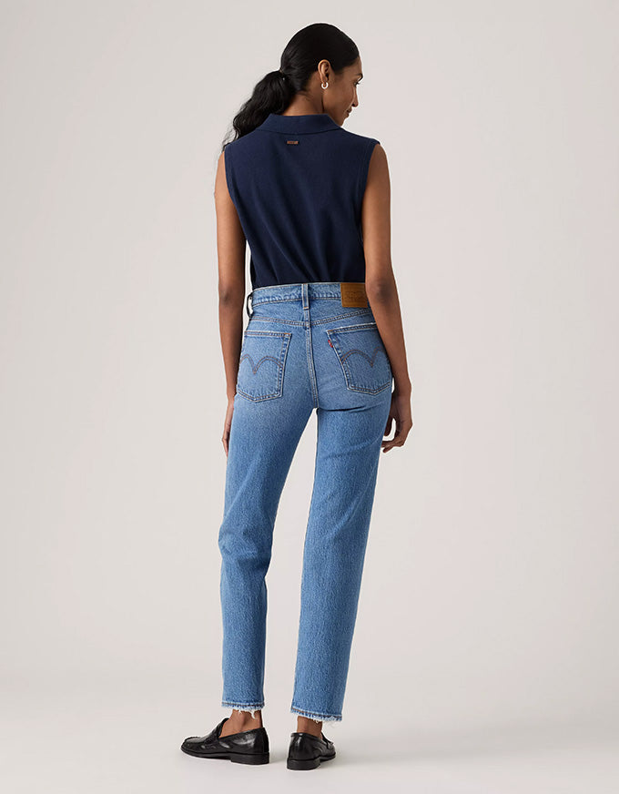 A model is shown from the back wearing a navy sleeveless top, light blue high-waisted jeans with a brown leather belt, and black leather loafers, set against a plain light gray studio background.