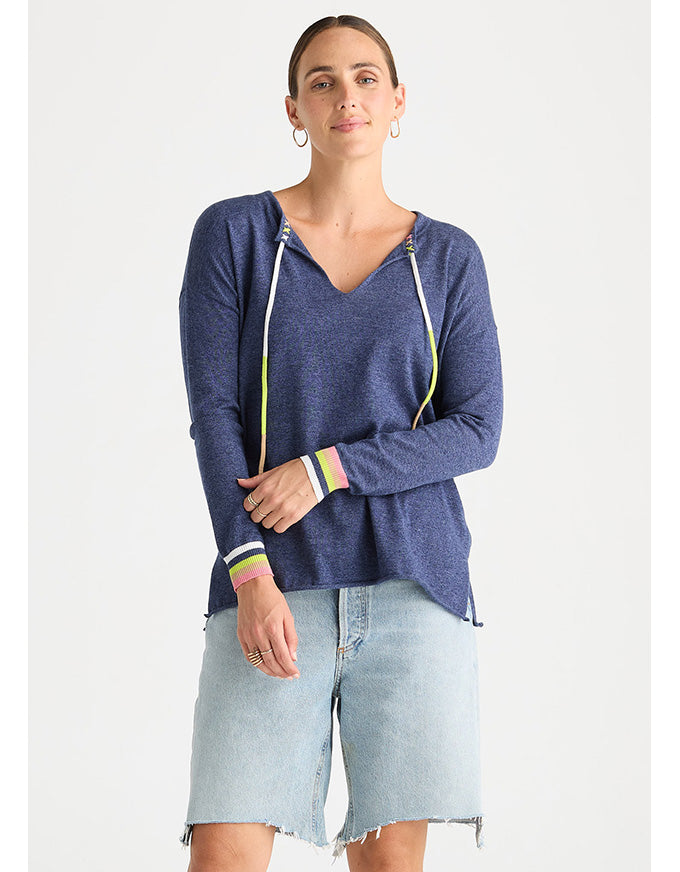 A woman modeling a heathered blue long-sleeve hoodie with colorful striped drawstrings and cuffs, paired with light-wash denim shorts, against a plain light gray background.