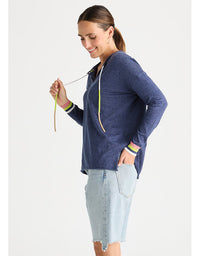 A woman wearing a navy blue heathered hoodie with green and white striped cuffs, paired with a light wash denim skirt, photographed against a solid off-white background.