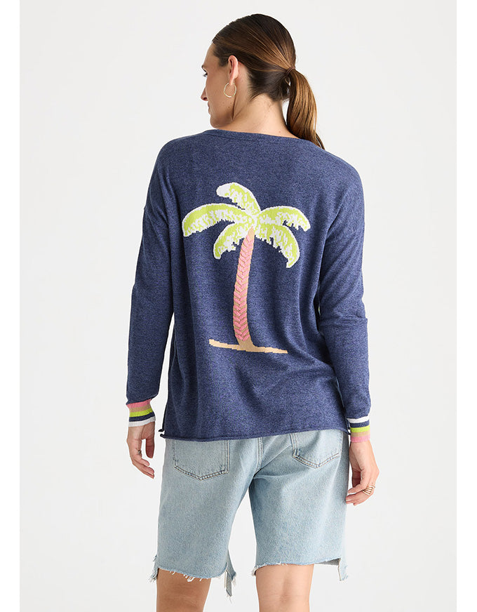 A woman shown from the back wearing a heathered navy blue long-sleeve top with a large sequined palm tree graphic on the back, paired with light-wash denim shorts, against a plain light gray background.