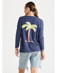 A woman shown from the back wearing a heathered navy blue long-sleeve top with a large sequined palm tree graphic on the back, paired with light-wash denim shorts, against a plain light gray background.