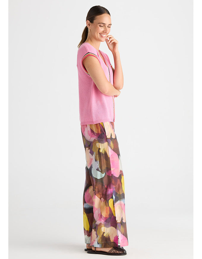 A woman modeling a pink sleeveless knit vest and wide-leg pants with a colorful abstract floral print, standing against a light gray studio background. Crochet Trim Tank - Begonia Park