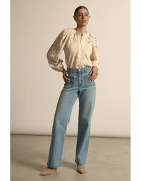 Woman wearing a beige blouse and blue jeans against a neutral background