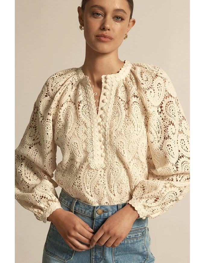Woman wearing a beige lace blouse and blue jeans against a neutral background