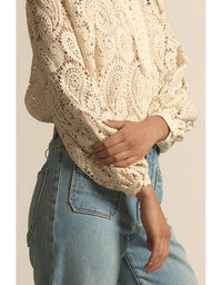 Person wearing a cream lace top and blue jeans against a neutral background