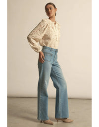 Woman wearing a lace blouse and blue jeans against a neutral background