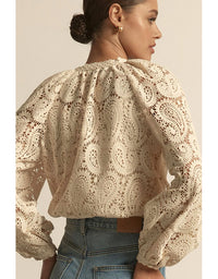 Woman wearing a beige lace blouse with long sleeves on a plain background