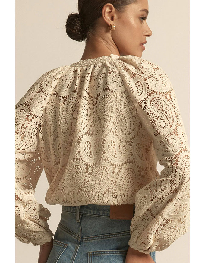 Woman wearing a beige lace blouse with long sleeves on a plain background