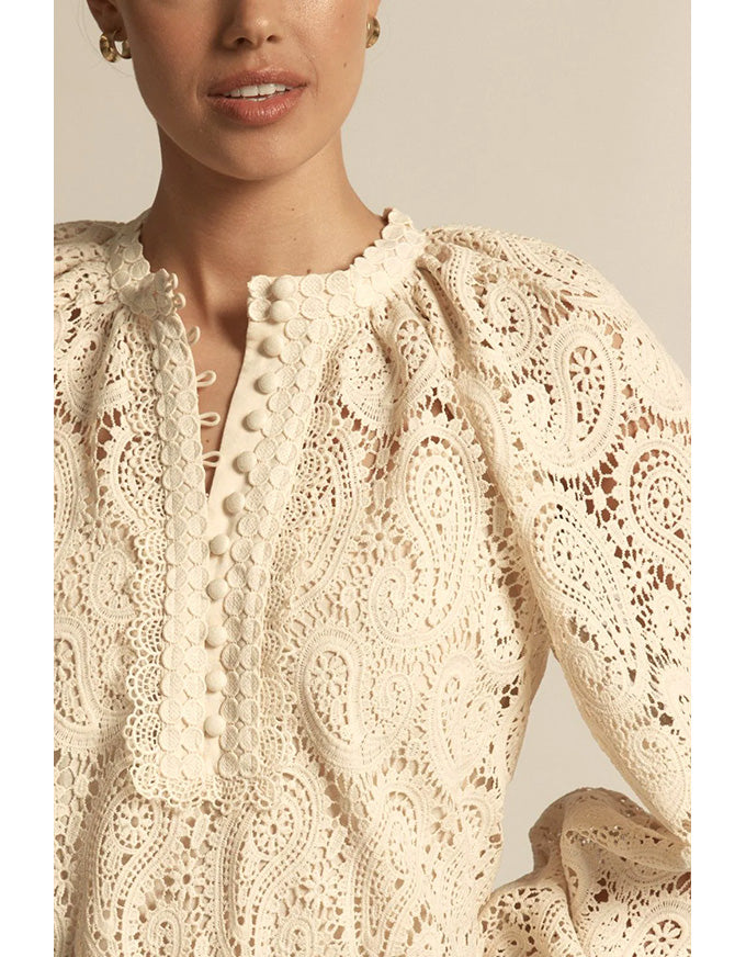 Close-up of a person wearing a cream-colored lace top with a neutral background