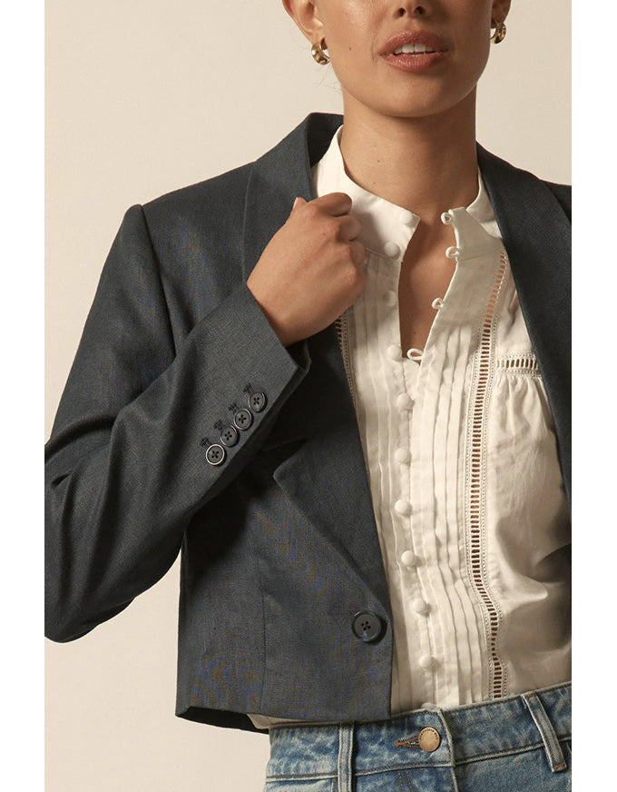 Person wearing a dark blazer over a white shirt with a beige background