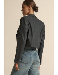 Person wearing a dark denim jacket and light blue jeans on a beige background