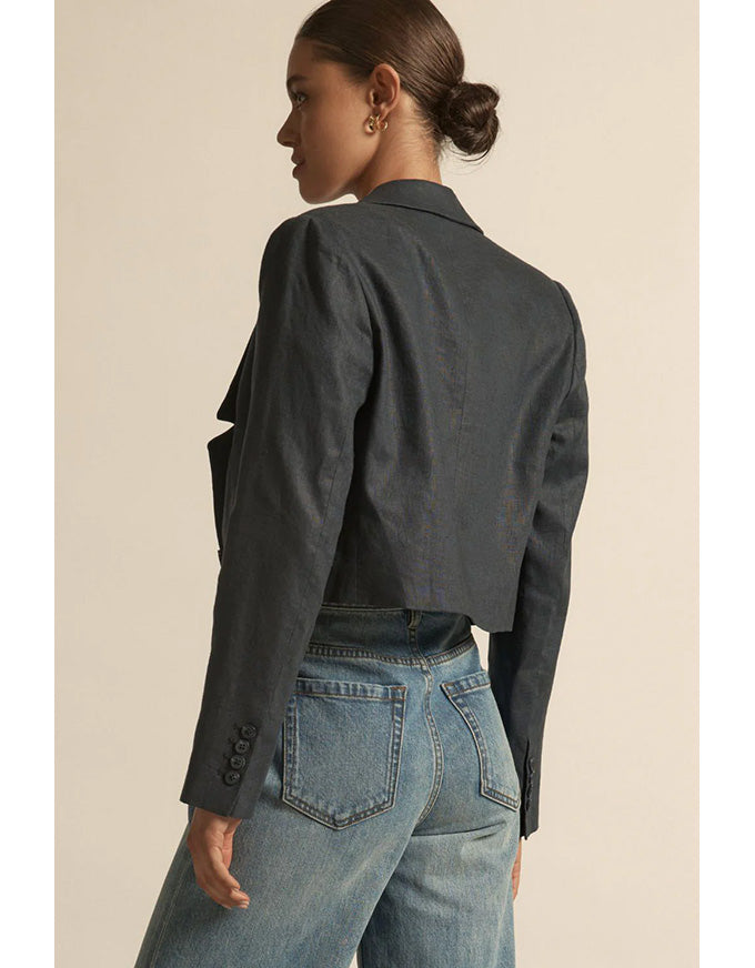 Person wearing a dark denim jacket and light blue jeans on a beige background