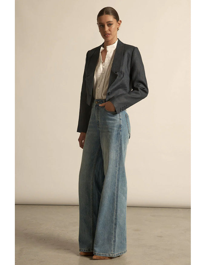 Woman wearing a black jacket and blue jeans against a plain background