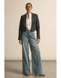 Woman wearing a navy blazer, white blouse, and blue jeans against a beige background