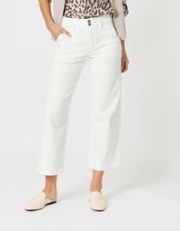 A model wearing a pair of white cropped wide-leg jeans, styled with a leopard-print top, a light beige cardigan, and cream-colored loafers, set against a plain light gray studio background.