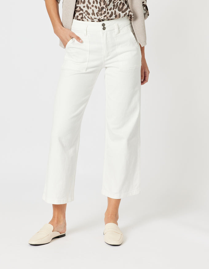 A model wearing a pair of white cropped wide-leg jeans, styled with a leopard-print top, a light beige cardigan, and cream-colored loafers, set against a plain light gray studio background.