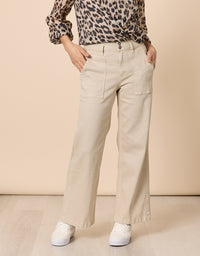 A person wearing beige wide-leg cargo pants with side pockets, paired with a leopard-print blouse and white sneakers, standing against a solid beige studio background.