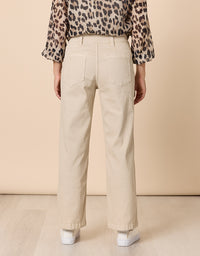 A person shown from the back wearing straight-leg beige jeans, a leopard-print blouse, and white sneakers against a plain beige studio background.