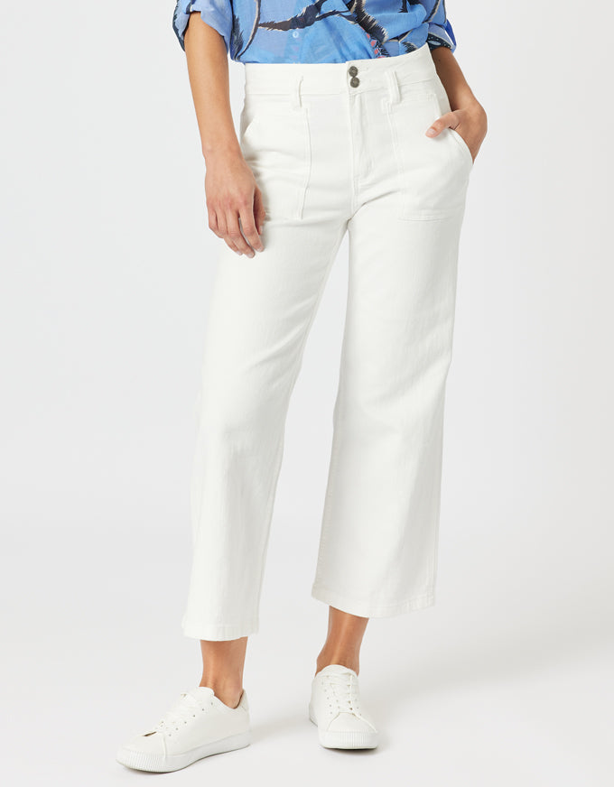 A model wearing a pair of white cropped wide-leg jeans with a blue patterned shirt and white sneakers, shown from the waist down on a light gray studio background.