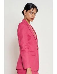 A woman wearing a bright pink tailored blazer and matching trousers, photographed in side profile against a plain light gray studio background. Crest Jacket Rhubarb