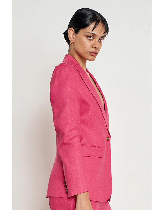 A woman wearing a bright pink tailored blazer and matching trousers, photographed in side profile against a plain light gray studio background. Crest Jacket Rhubarb