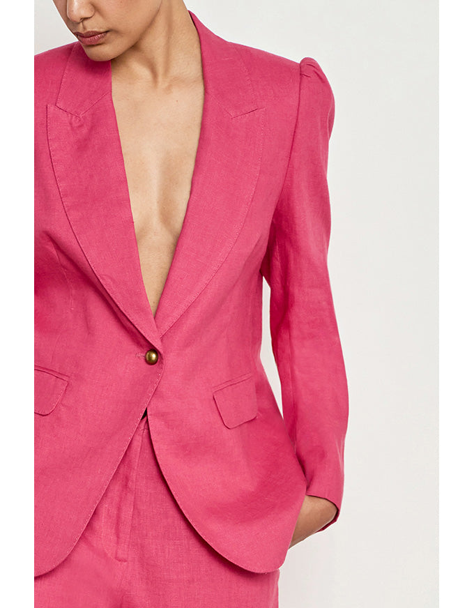 A close-up of a model wearing a bright pink tailored blazer with structured shoulders and a single button closure, paired with matching pink trousers against a plain light background. Crest Jacket Rhubarb