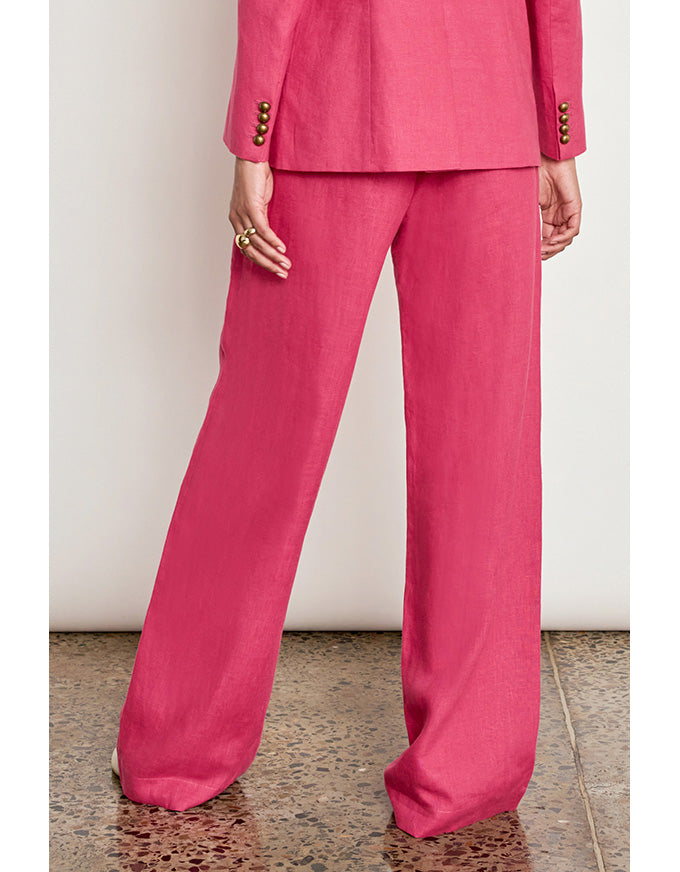 A person wearing a bright pink matching pants and blazer set, shown from the back against a plain light wall and speckled floor. Edit Pant Rhubarb