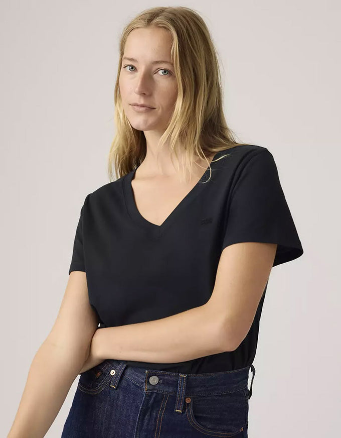 Woman wearing a black V-neck t-shirt and blue jeans against a light pink background
