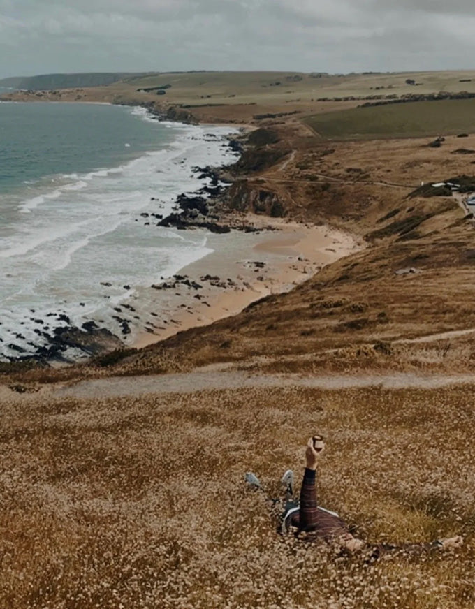 Two people walking along a coastal path with ocean and cliffs in the background