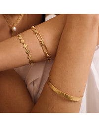 Two gold bracelets on a person's wrist against a neutral background