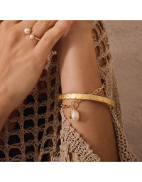 Gold bracelet with a pearl charm on a wrist against a textured fabric background