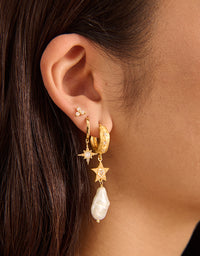 Close-up of an ear wearing gold hoop earrings with star and pearl details.