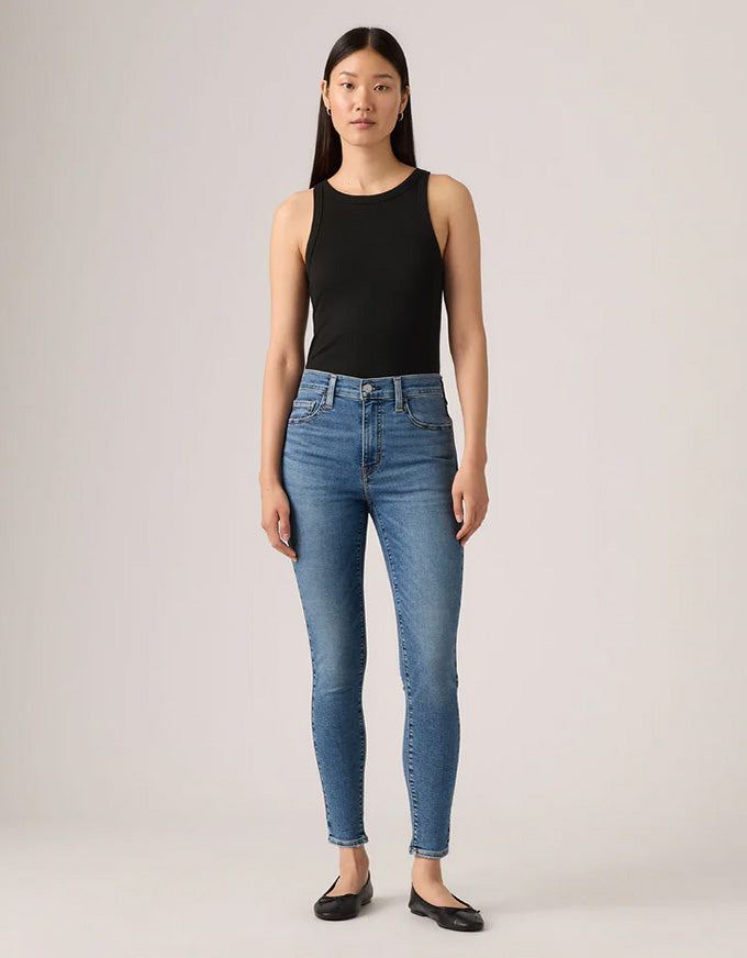 Woman wearing blue jeans and a black top on a plain background