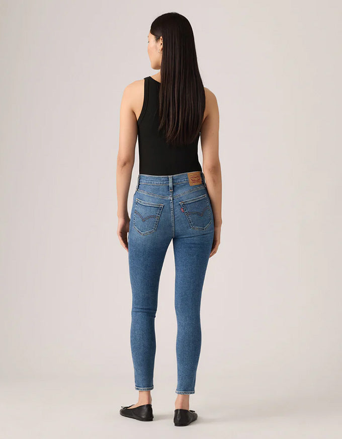 Woman wearing blue jeans with a visible brand logo on a plain background