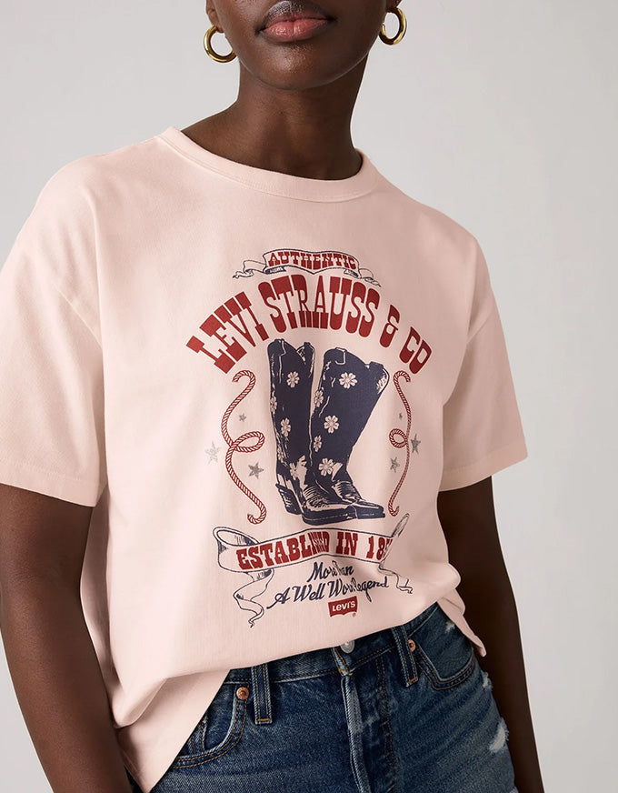 A close-up of a model wearing a light pink Levi's t-shirt with a western boot graphic and blue jeans.