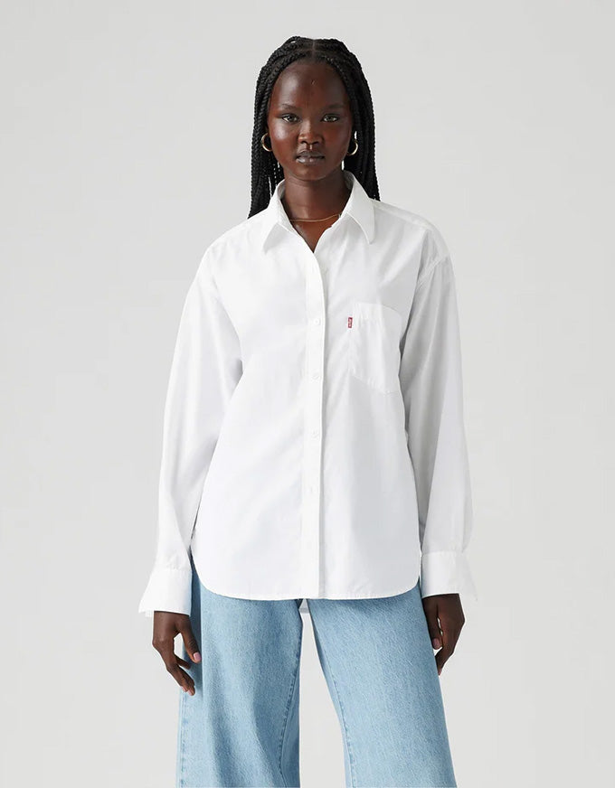 Woman wearing a white shirt with a small logo on a light gray background